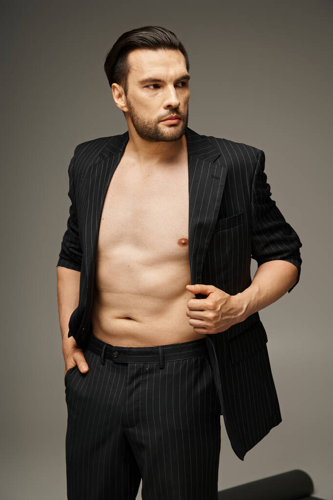 ファッションステートメントのコンセプト, グレーの背景にポーズピンストライプスーツの大胆でシャツレス男性 - 写真・画像