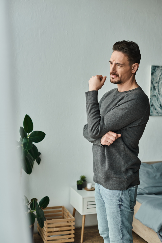 thoughtful and bearded man in grey jumper looking away while standing at home, deep in thought - Photo, Image