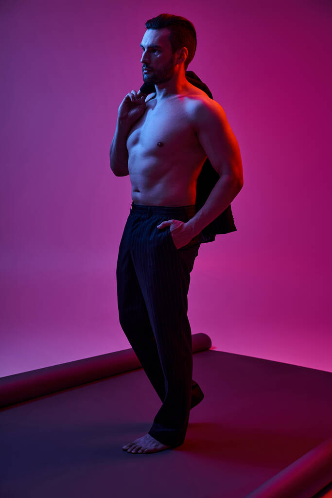 紫色のポケットに手でポケットをポーズしながら,裸の胸とブリストルを持つシャツレスの男 - 写真・画像