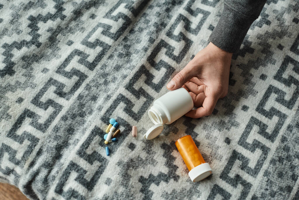 обрізана фотографія чоловічої руки, що досягає пляшки з ліками на сірій ковдрі з орнаментом, таблетки - Фото, зображення