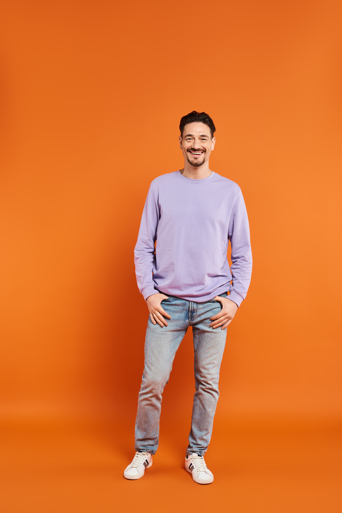 full length of cheerful and bearded man in purple sweater looking at camera on orange background - Photo, Image