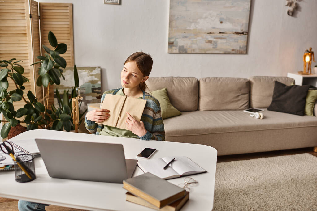 tiener meisje holding boek en het gebruik van laptop tijdens video gesprek thuis, gen z lifestyle concept - Foto, afbeelding