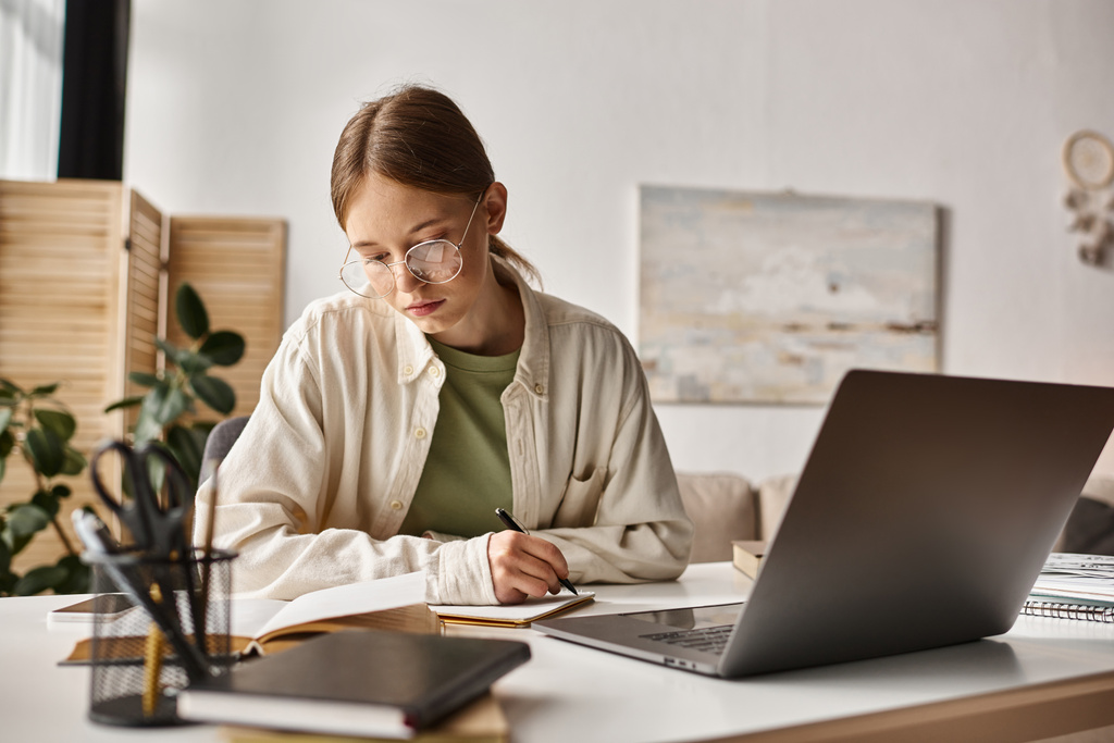 adolescente em óculos segurando caneta e escrevendo durante a aula on-line no laptop, tomando notas - Foto, Imagem