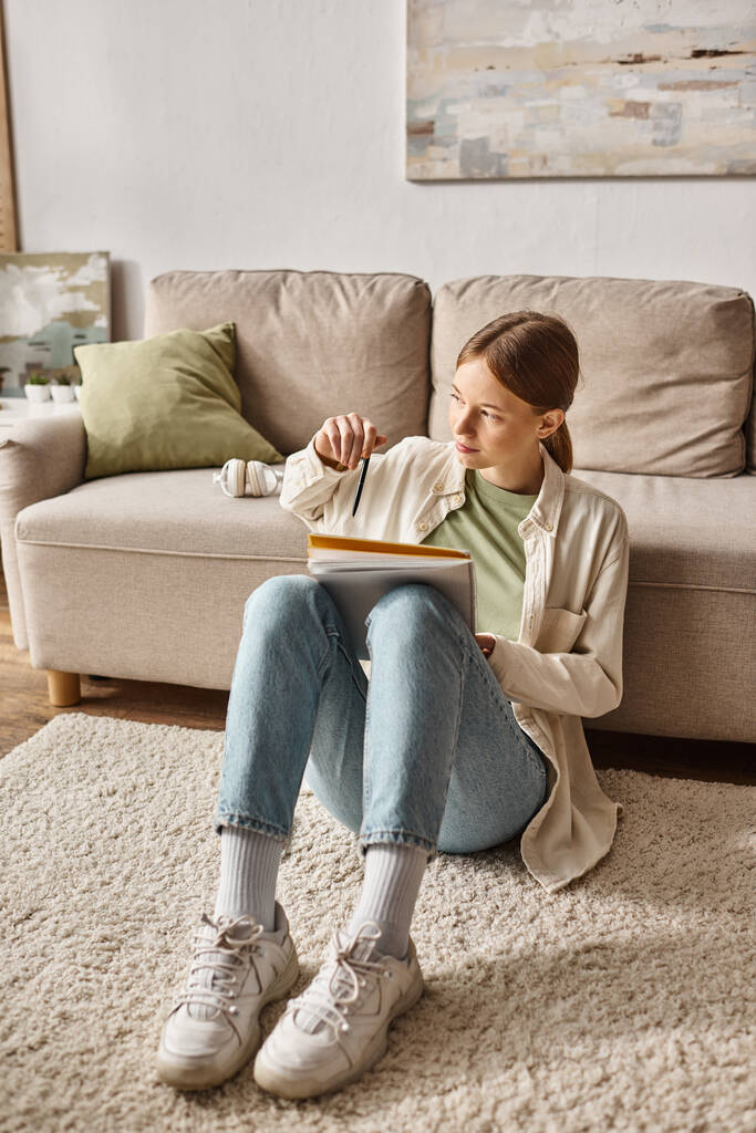 Pensive дівчина-підліток читає свій блокнот і сидить біля дивана з навушниками поблизу - Фото, зображення