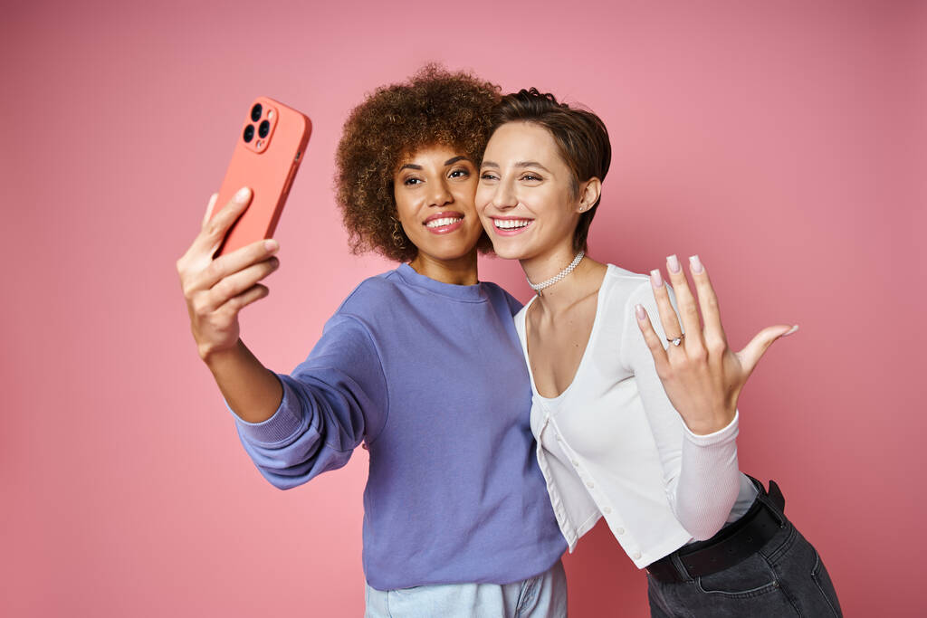 boldog leszbikus nő mutatja eljegyzési gyűrű az ujján, miközben szelfi menyasszonya rózsaszín - Fotó, kép