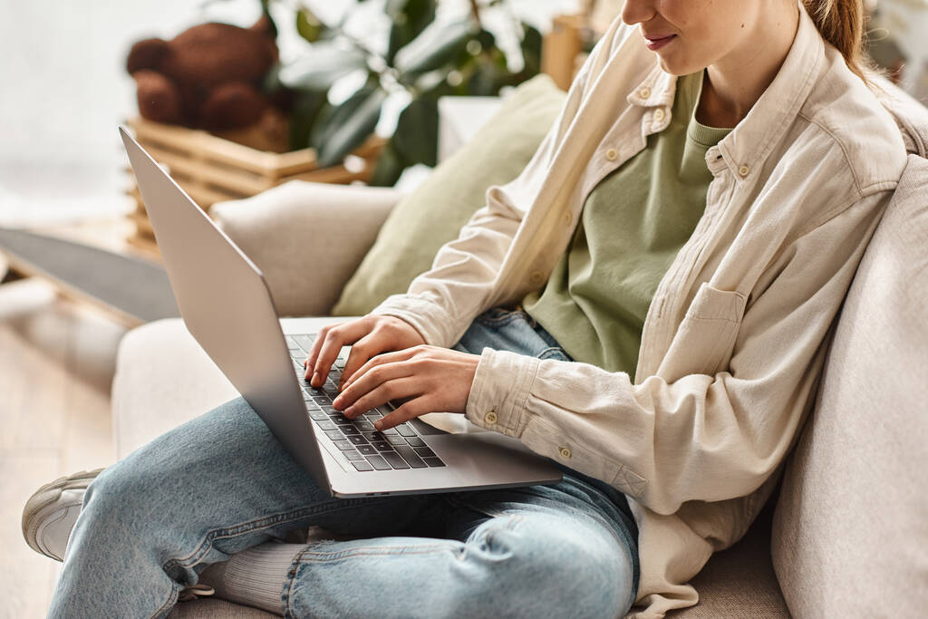 обрізана дівчина-підліток зосередилася на електронному навчанні, використовуючи ноутбук і сидячи на зручному дивані вдома - Фото, зображення