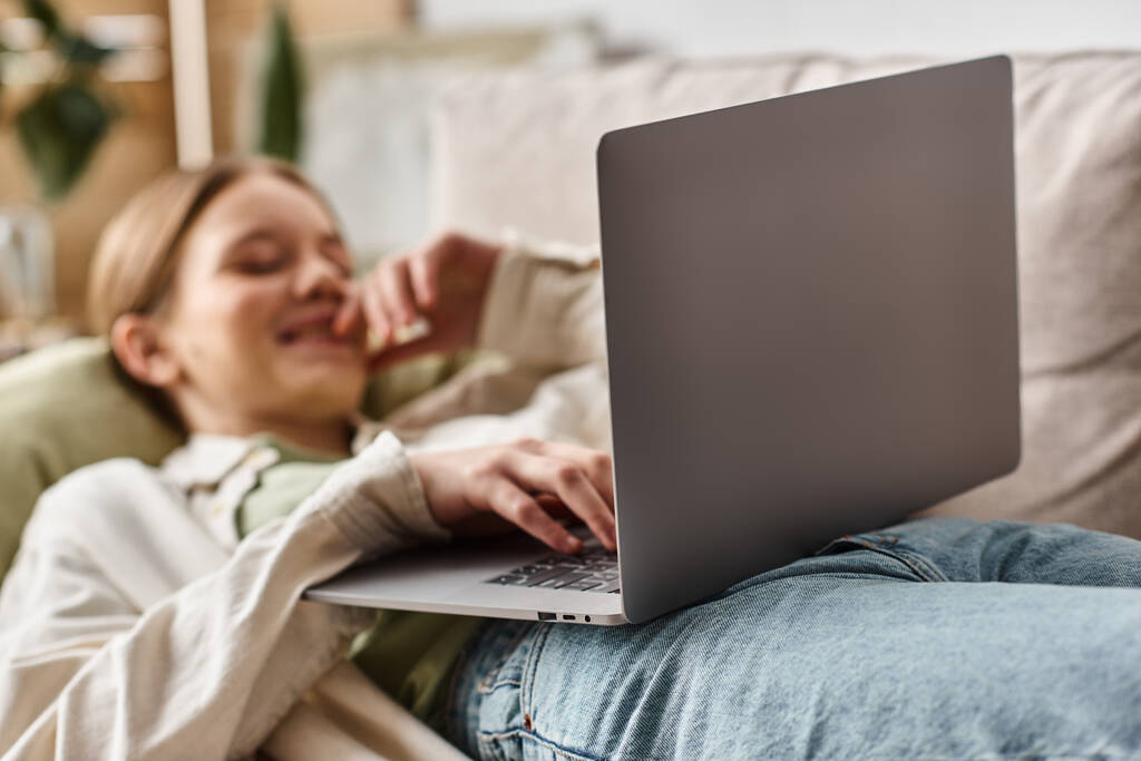 focus on laptop, happy teenage generation z girl lying on sofa and using her laptop at home - Photo, Image