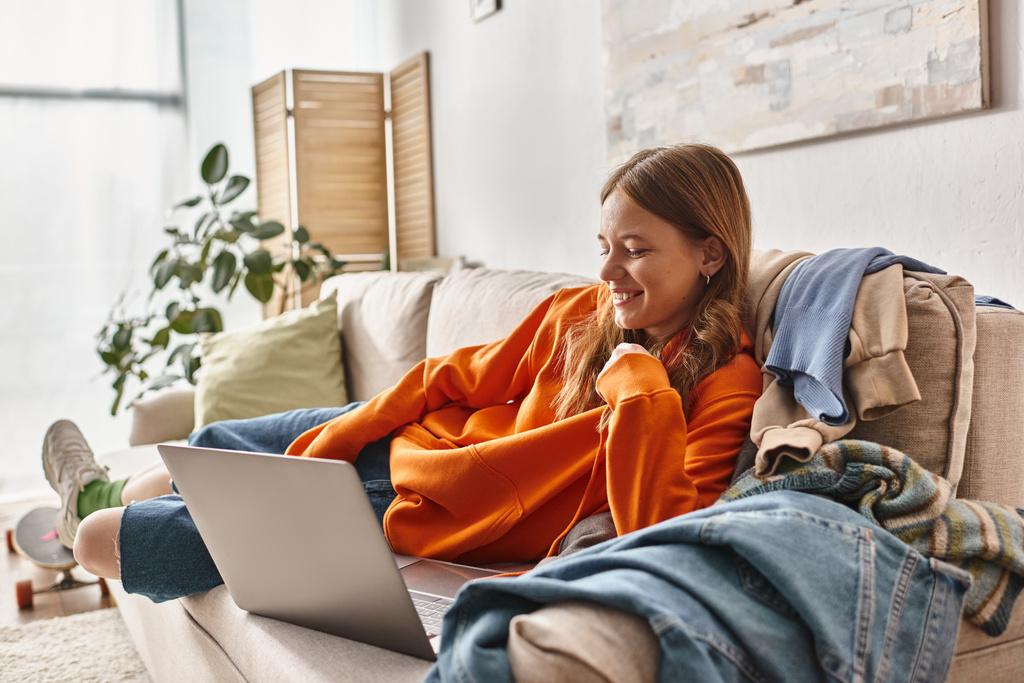 gelukkig tiener meisje kijken naar een film op een laptop terwijl ontspannen op een bank in de woonkamer, vrije tijd - Foto, afbeelding