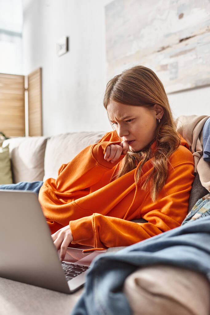 сфокусированная девочка-подросток смотрит фильм на ноутбуке, расслабляясь на диване в гостиной, досуге - Фото, изображение