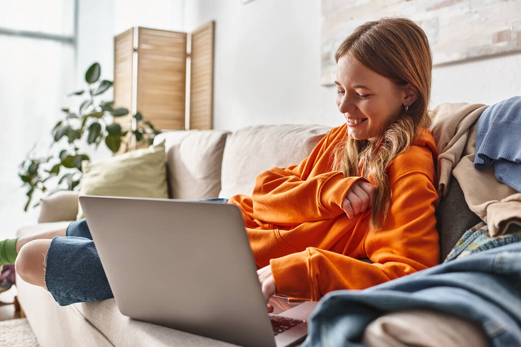 felice adolescente ragazza guardando film commedia su un computer portatile mentre si rilassa su un divano in soggiorno - Foto, immagini