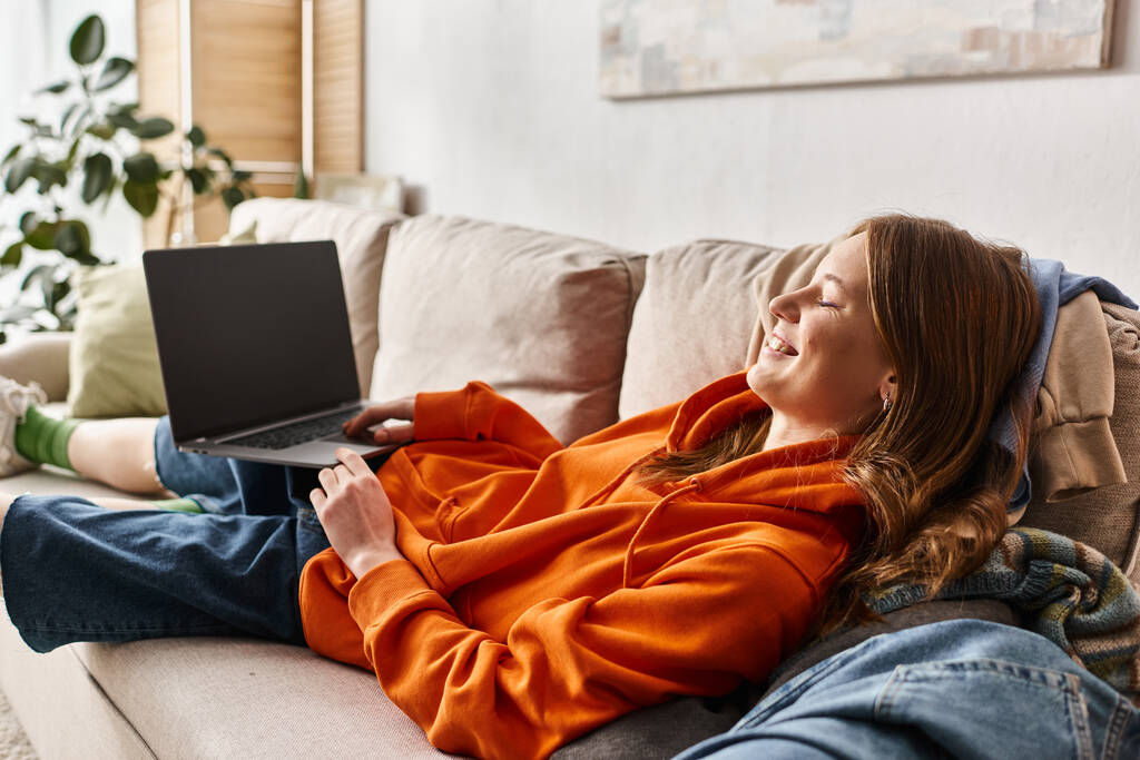 szczęśliwy nastolatek dziewczyna oglądanie komedia film na laptopie z pusty ekran podczas relaks na kanapie - Zdjęcie, obraz