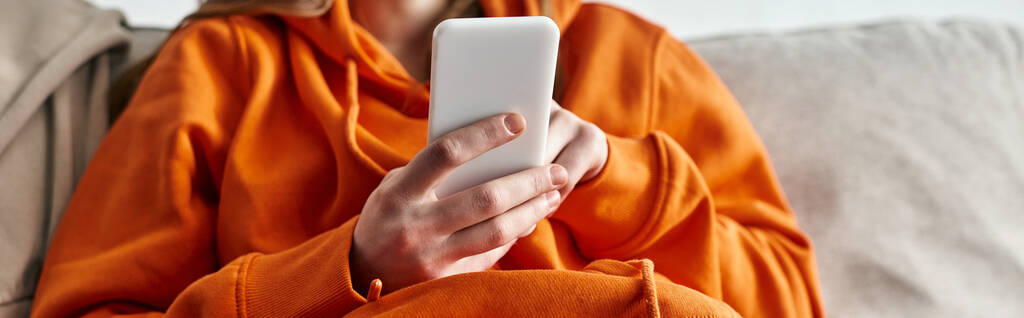 bijgesneden weergave van tiener browsen smartphone en zitten op de bank thuis, horizontale banner - Foto, afbeelding