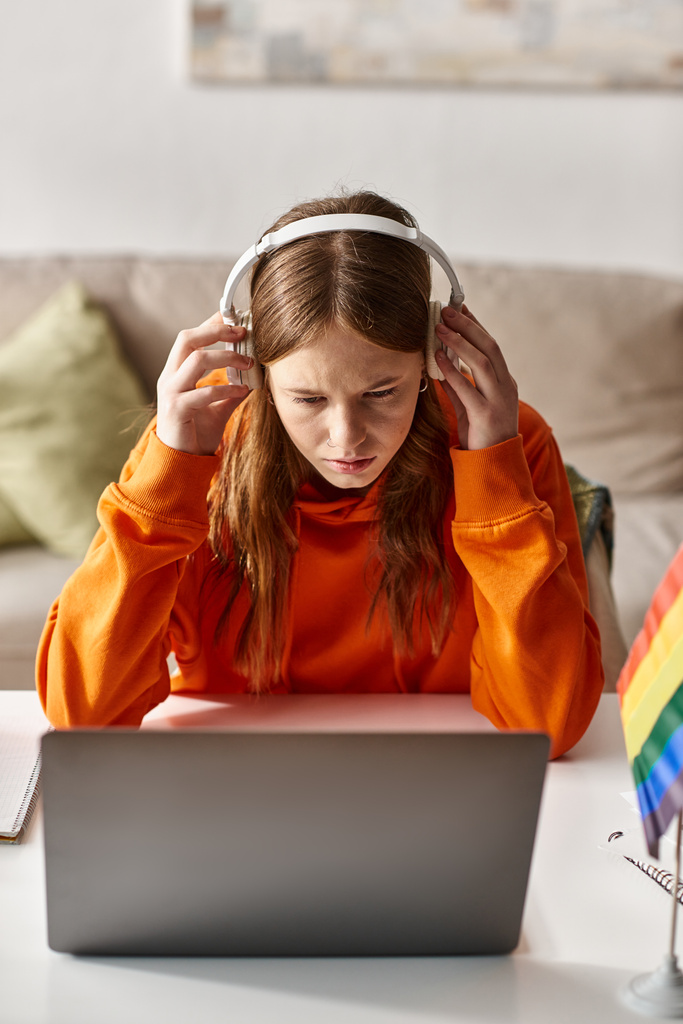 adolescente con sus auriculares y e-learning al lado de la computadora portátil y bandera de orgullo en el escritorio - Foto, imagen