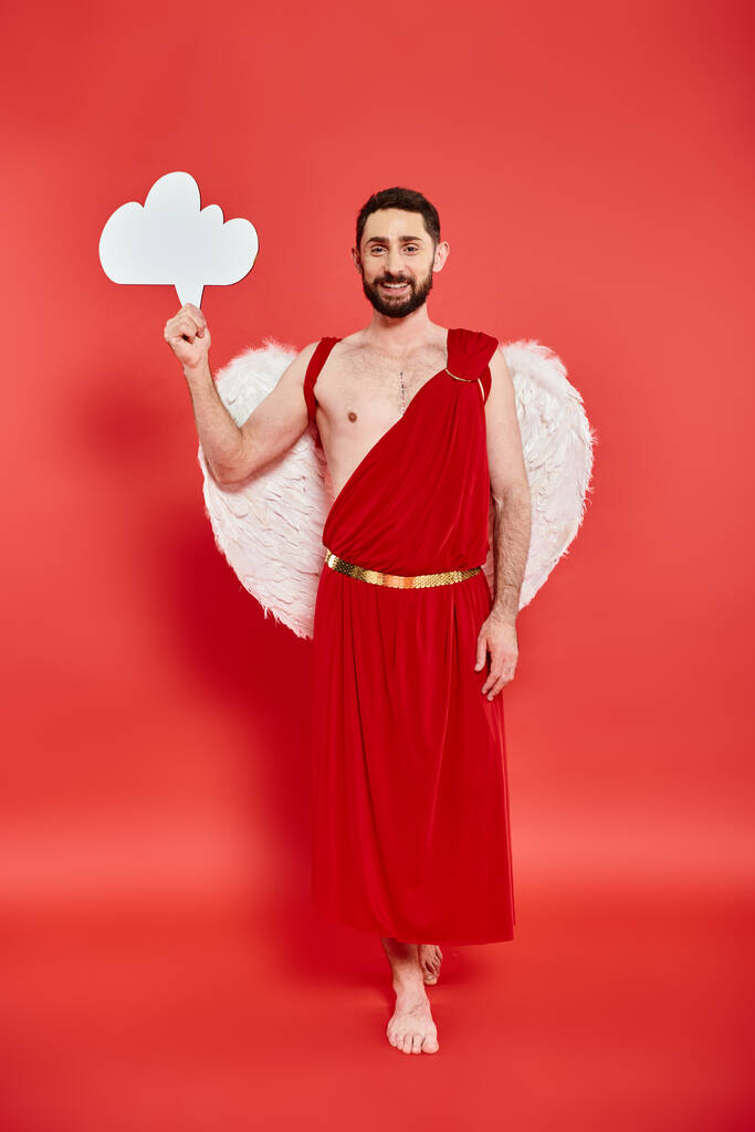 full length of barefoot bearded man dressed as cupid with white empty thought bubble on red - Photo, Image