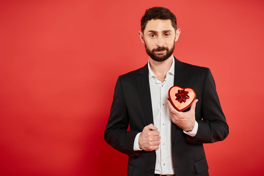 elégedett szakállas üzletember fekete öltöny szív alakú ajándék doboz piros, Szent Valentin nap - Fotó, kép