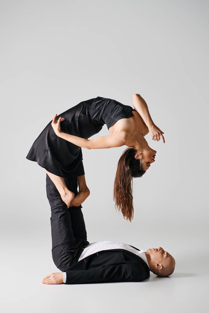 mulher flexível em traje preto equilibrando em pés descalços de seu parceiro de dança em pano de fundo cinza - Foto, Imagem