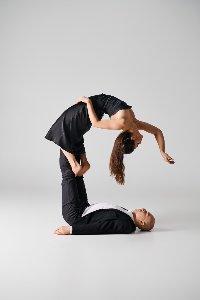 flexible young woman in black dress balancing on bare feet of her dancing partner on grey backdrop - Photo, Image