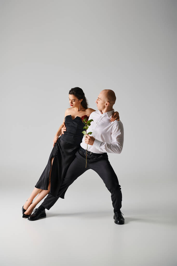 Elegantní taneční pohyb mladých tanečnic, ženy držící rudou růži a muže ve formálním oděvu ve studiu - Fotografie, Obrázek