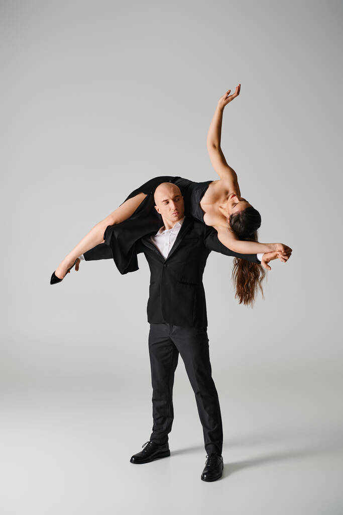 forte danseuse masculine soulevant femme brune en robe et talons hauts en studio sur fond gris - Photo, image