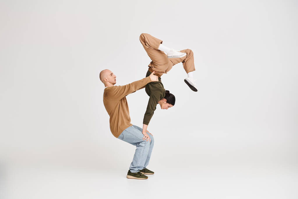 Casal em traje casual realizando um equilíbrio acrobático intrincado em estúdio em fundo cinza - Foto, Imagem