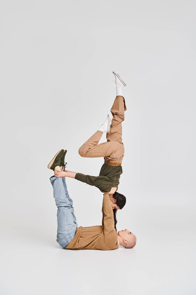 Couple acrobatique, jeune femme brune en tenue décontractée équilibrage avec le soutien de partenaire en studio - Photo, image
