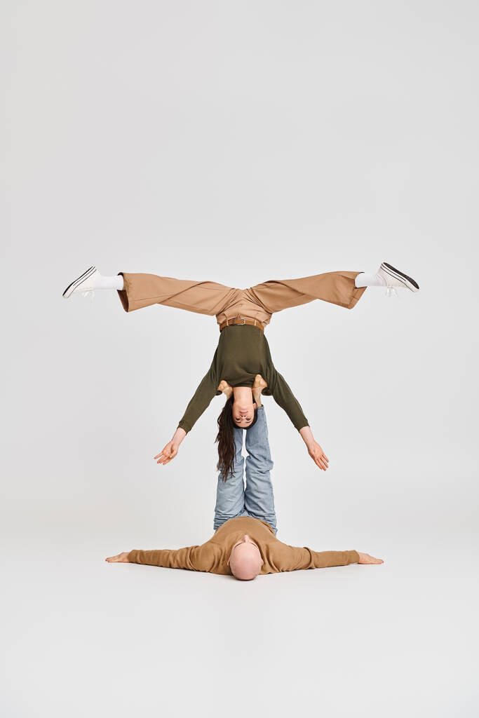 артистическая пара, акробатка, держащая равновесие вверх ногами при поддержке мужчины в серой студии - Фото, изображение