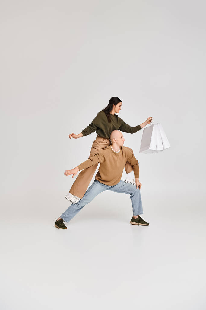 akrobatyczne wykonanie pary artystycznej, kobieta z torbami na zakupy balansująca na ciele mężczyzny na szarości - Zdjęcie, obraz