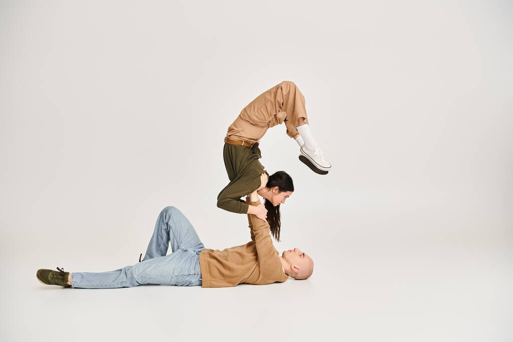 молода брюнетка в повсякденному носінні балансує на руках сильного чоловіка, пара акробатів в студії - Фото, зображення