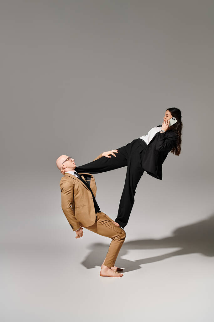 бизнесвумен со смартфоном звонит и балансирует с помощью мужчины на сером, пара акробатов - Фото, изображение