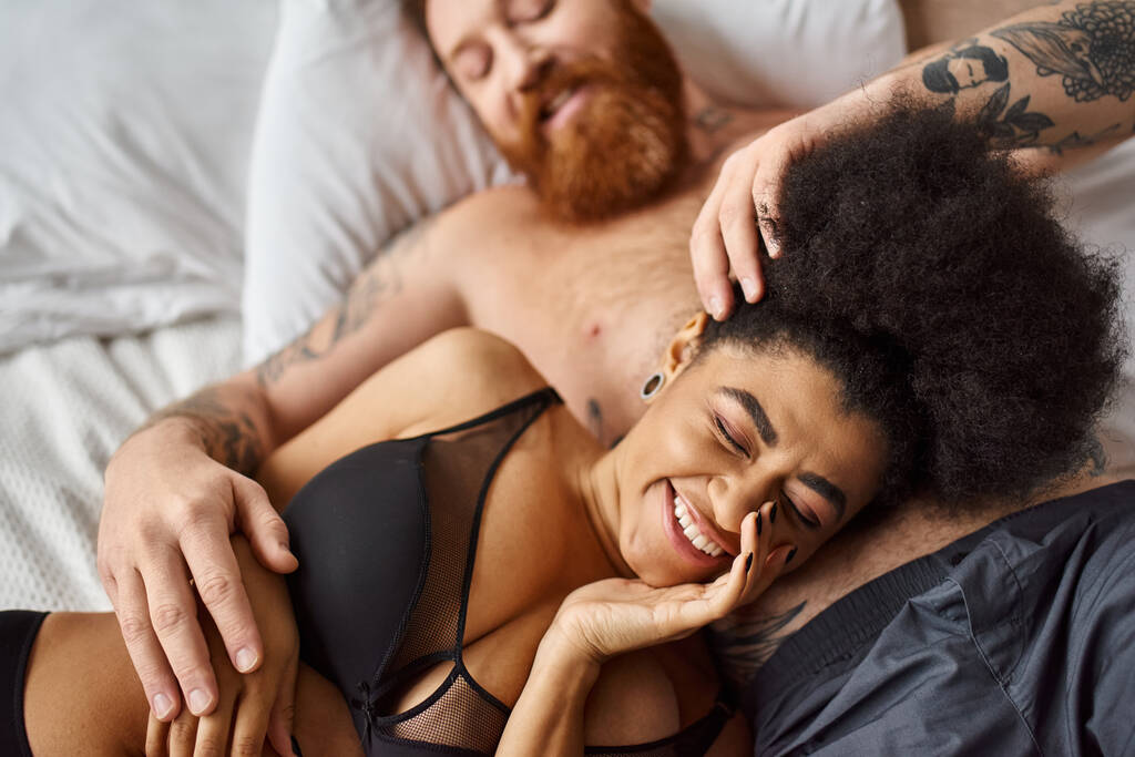 mosolygós és göndör afro-amerikai nő fehérneműben fekszik mellette a férfi a hálószobában, lelki társak - Fotó, kép