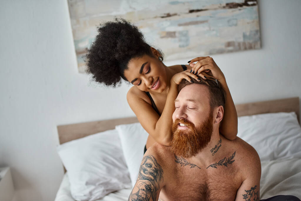 szexi változatos pár, vidám göndör afro-amerikai nő elcsábítja neki tetovált férfi a hálószobában - Fotó, kép