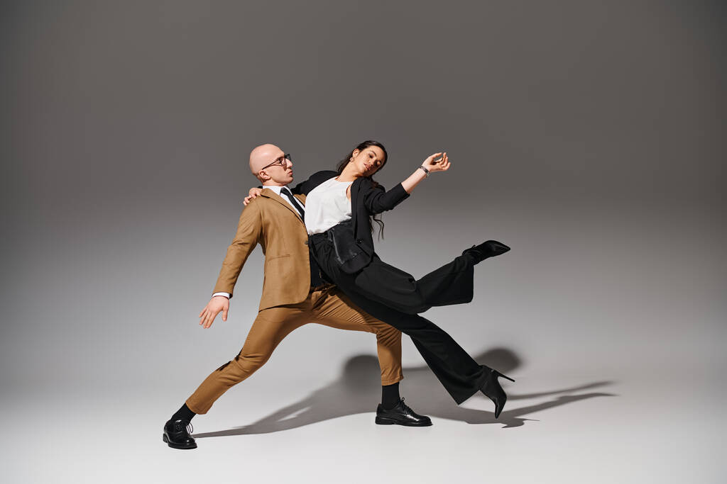 Geschäftspaar in stylischen Anzügen in kreativer akrobatischer Pose, Mann unterstützt Frau im Studio - Foto, Bild
