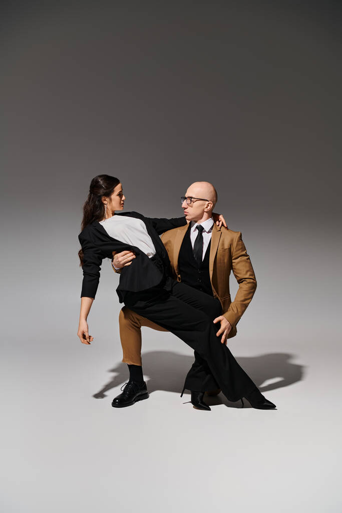 mężczyzna w garniturze i okulary wspieranie brunetka podczas tańca w studio na szary - Zdjęcie, obraz