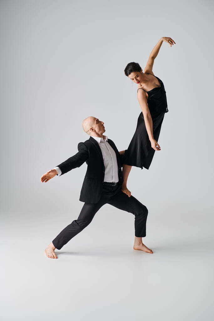boso kobieta w czarnej sukience balansowanie wdzięcznie na kolanach partnera tanecznego w szarym studio - Zdjęcie, obraz