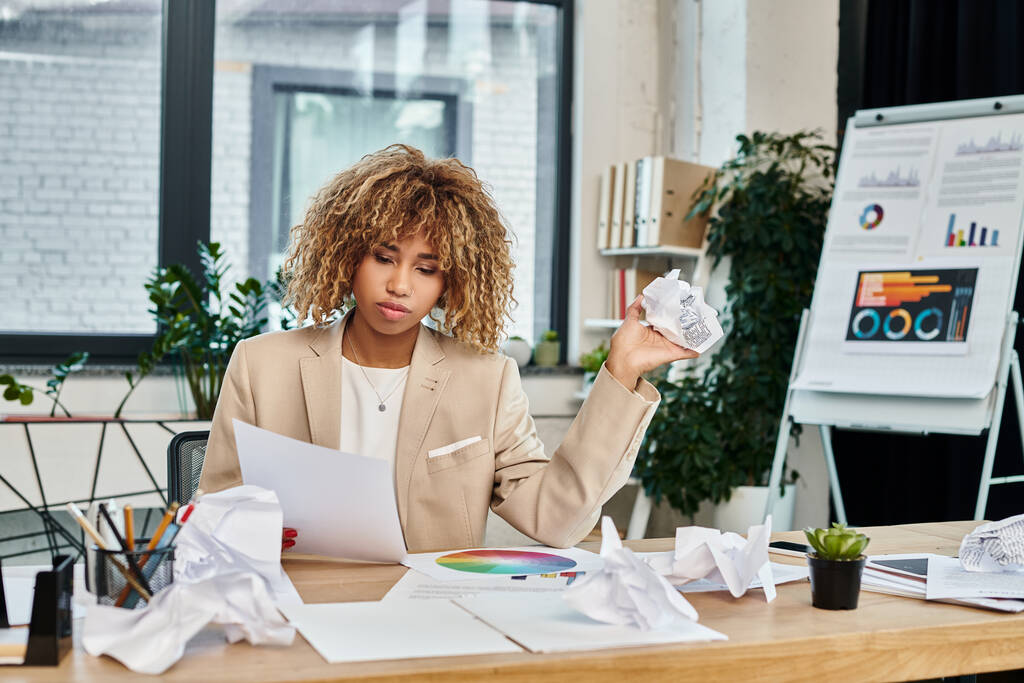 zamyślony kręcone afrykański biznes amerykański kobieta przy jej biurku i trzyma pogniecione papiery, stres - Zdjęcie, obraz