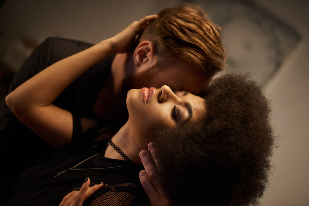γενειοφόρος άντρας φιλάει σέξι αφροαμερικανή γυναίκα με σγουρά μαλλιά, πολυπολιτισμικό καυτό ζευγάρι - Φωτογραφία, εικόνα