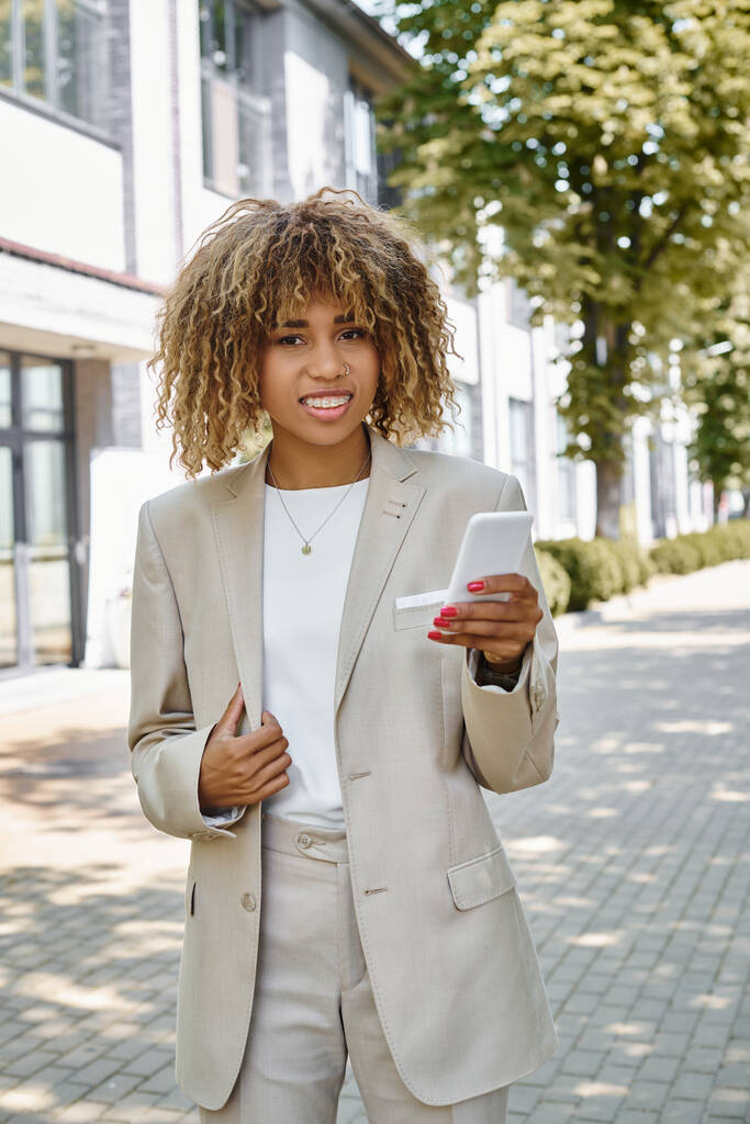 オフィスビルの近くで彼女のスマートフォンを使用してブレースで幸せなアフリカ系アメリカ人起業家 - 写真・画像