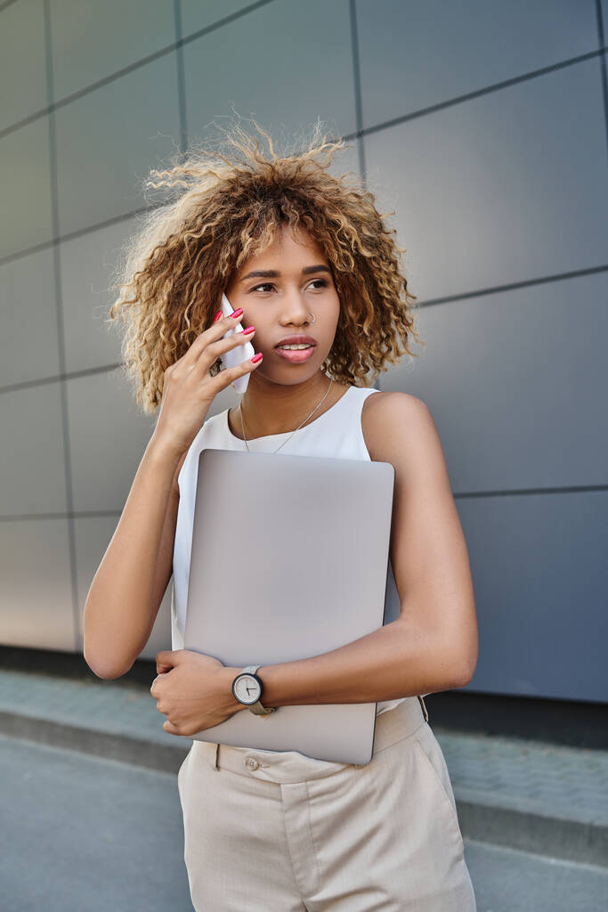 Modern fiatal professzionális, afro-amerikai nő laptoppal, hogy egy hívást szürke fal - Fotó, kép