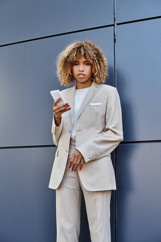 молода і проколота афроамериканська бізнес-леді з кучерявим волоссям тримає свій смартфон на відкритому повітрі - Фото, зображення