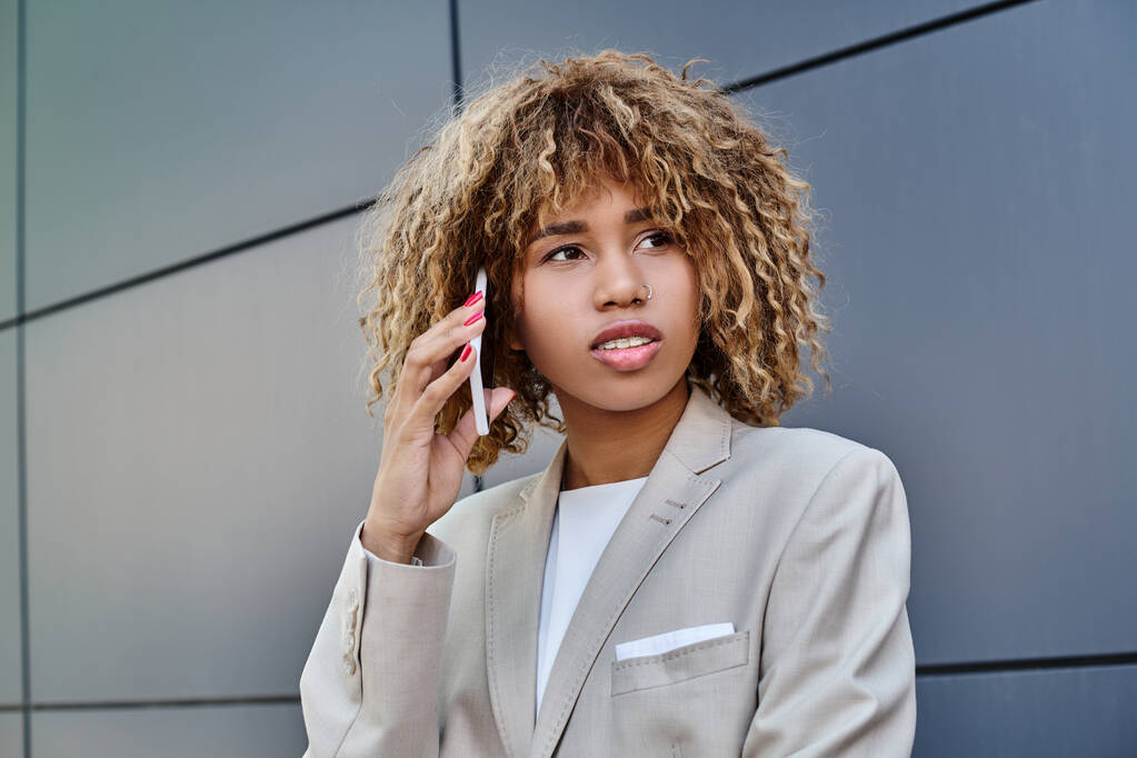 mujer de negocios afroamericana pensativa y joven con el pelo rizado hablando en el teléfono inteligente fuera - Foto, imagen