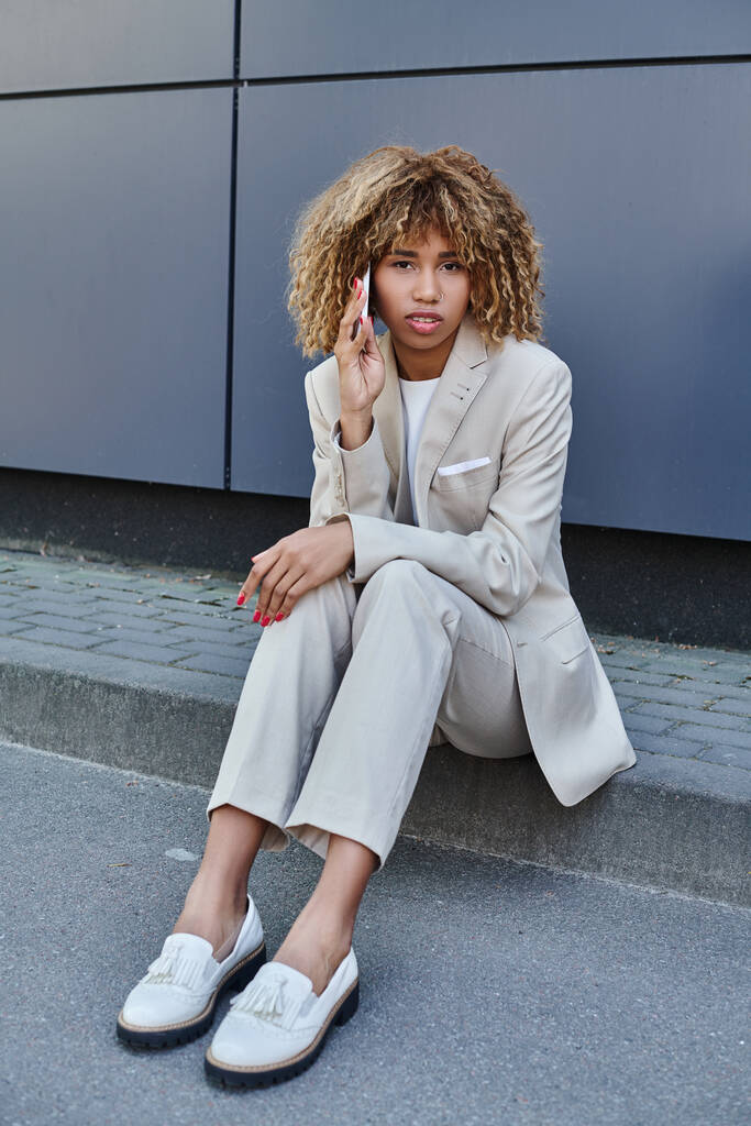 giovane donna d'affari afroamericana in giacca e cravatta seduta sul parapetto e parlare sul suo smartphone - Foto, immagini