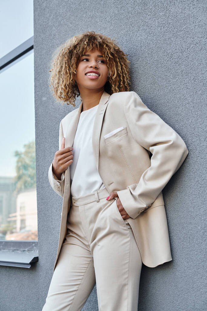 joven y positiva mujer de negocios afroamericana en ropa formal de pie con la mano en el bolsillo al aire libre - Foto, Imagen