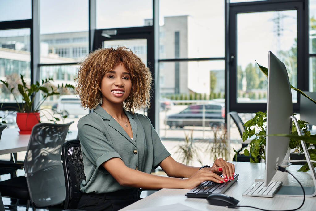 heureuse jeune femme d'affaires afro-américaine assise au bureau devant un écran d'ordinateur au bureau - Photo, image