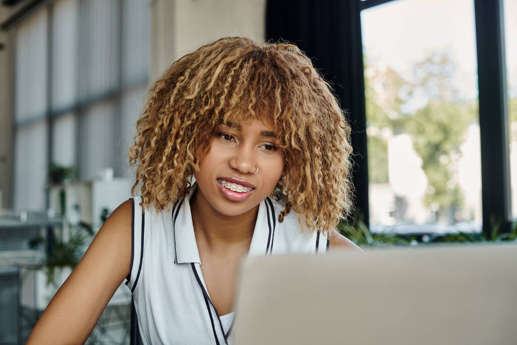 счастливая африканская американская деловая женщина с дружелюбной улыбкой во время видеозвонка на ноутбук в офисе - Фото, изображение