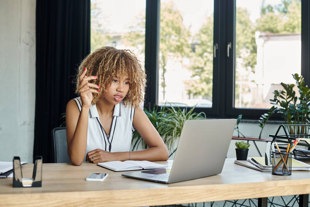 jeune femme d'affaires afro-américaine gestuelle lors d'un appel vidéo sur un ordinateur portable près du smartphone sur le bureau - Photo, image