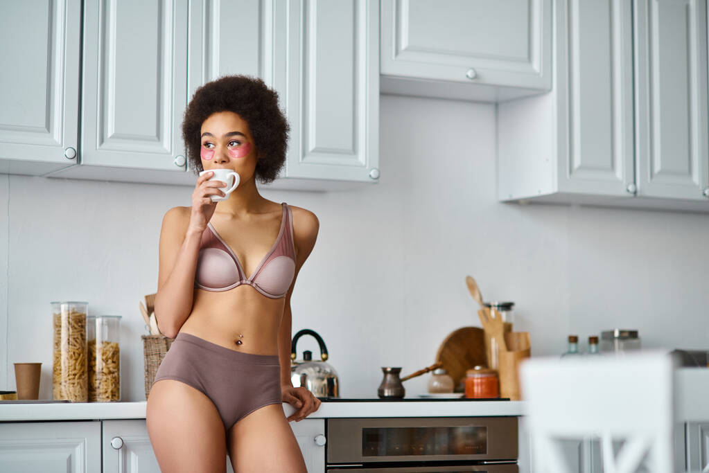 femme afro-américaine bouclée avec des patchs debout dans les sous-vêtements et boire du café de tasse - Photo, image