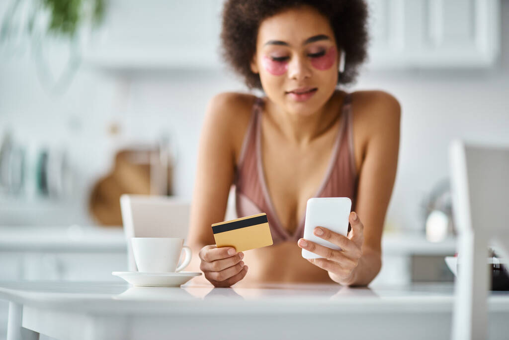 mulher americana africana alegre compras on-line com cartão de crédito e smartphone na cozinha - Foto, Imagem