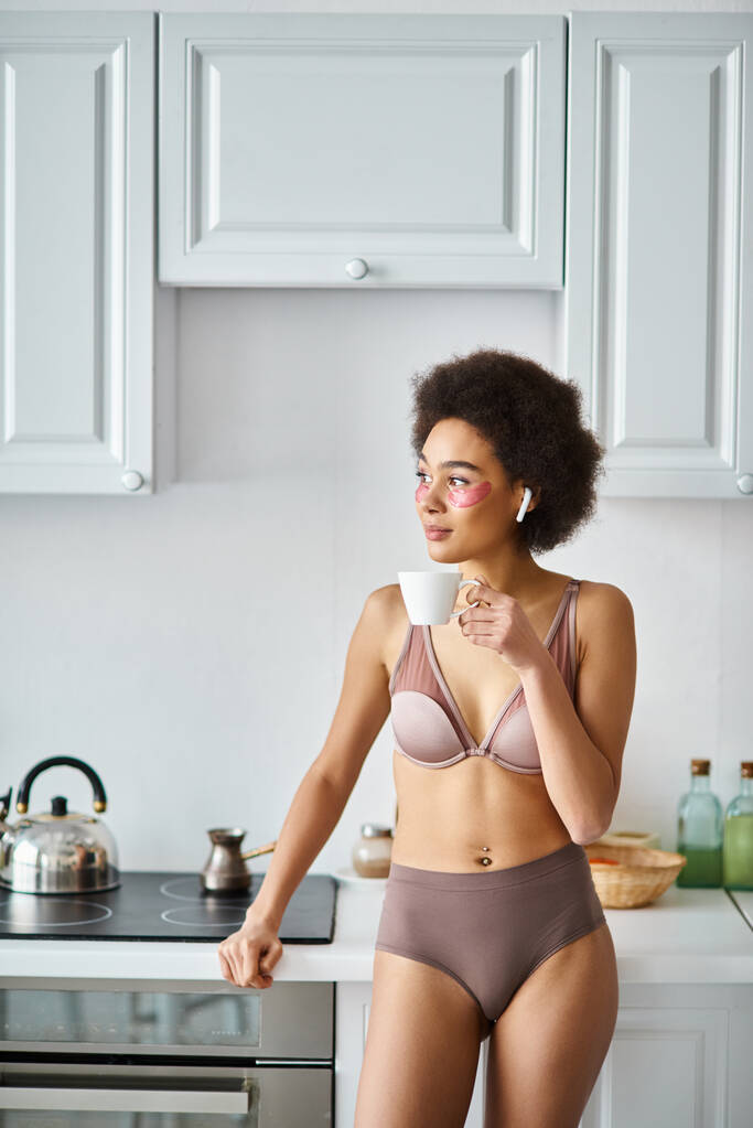 Klidný moment s africkou americkou ženou ve sluchátkách a spodní prádlo popíjení ranní kávy - Fotografie, Obrázek