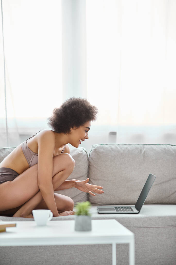щаслива афроамериканка в нижній білизні сидить на дивані і використовує ноутбук вдома, розваги - Фото, зображення