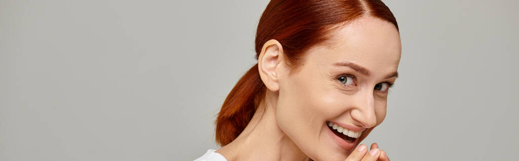 astonished and redhead woman in white tank top laughing a grey background, radiant smile banner - Photo, Image